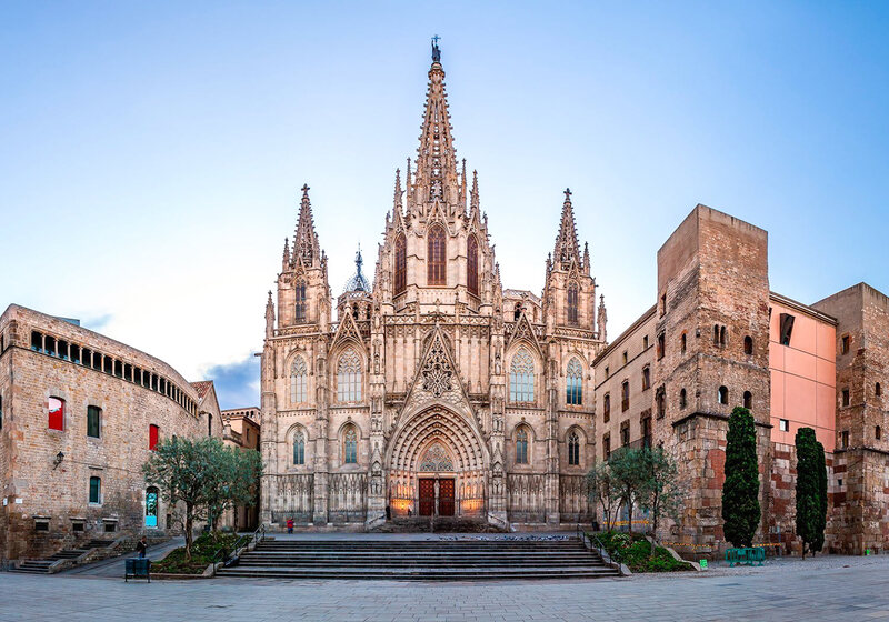 The majestic Barcelona Cathedral stands as a centerpiece in the Gothic Quarter, with its intricate Gothic architecture and spires reaching towards the sky, flanked by historic stone buildings in the tranquil early morning light.