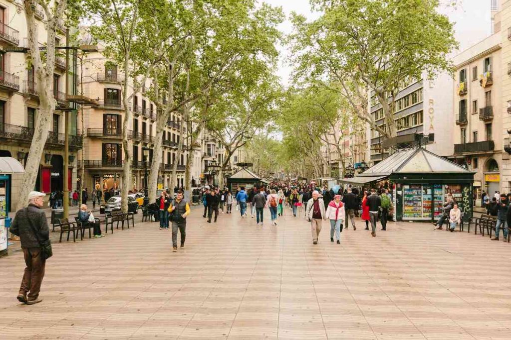 Pedestrians strolling down La Rambla, a bustling tree-lined street in the heart of Barcelona, flanked by historic buildings and local street vendors, showcasing the city's dynamic atmosphere.