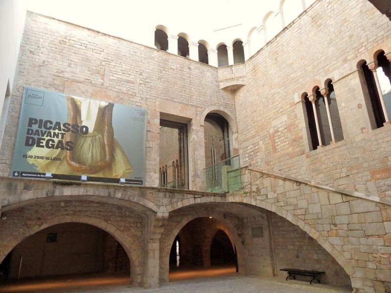 Interior courtyard of the Picasso Museum in Barcelona, showcasing the Gothic architecture with stone walls, arches, and a grand staircase, with a banner for the 'Picasso devant Degas' exhibition.