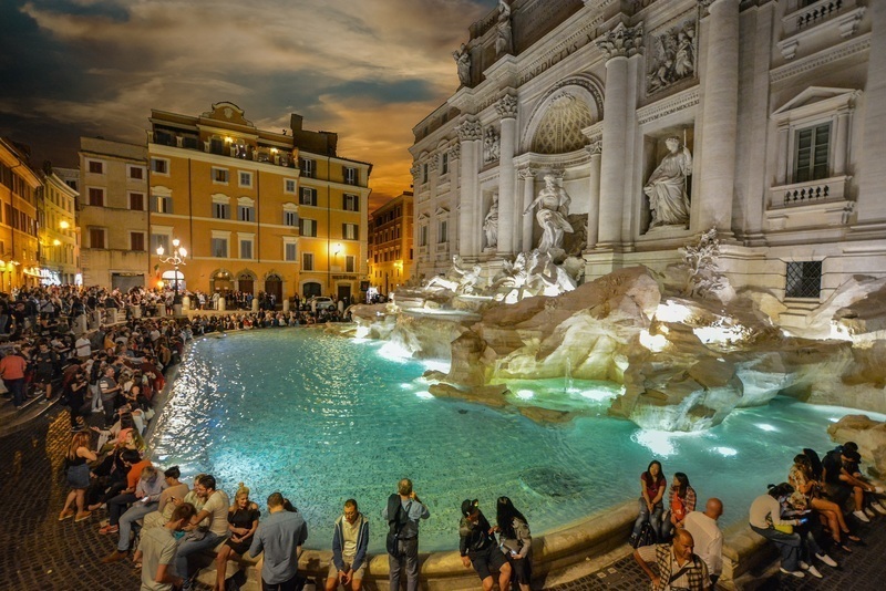 Crowds at night by Rome's glowing Trevi Fountain.