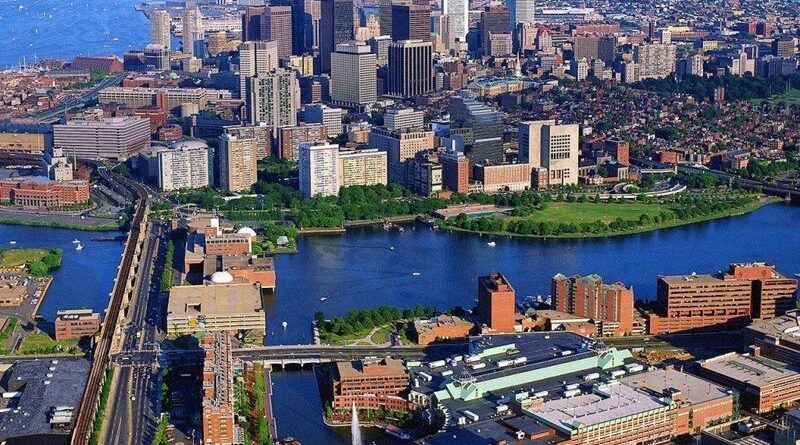 Aerial view of Boston showcasing its bustling downtown area with dense clusters of modern high-rises, the serene Charles River, and the intricate network of roads and bridges connecting diverse neighborhoods.